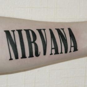 Фото тату на предплечье у парня с надписью Nirvana
